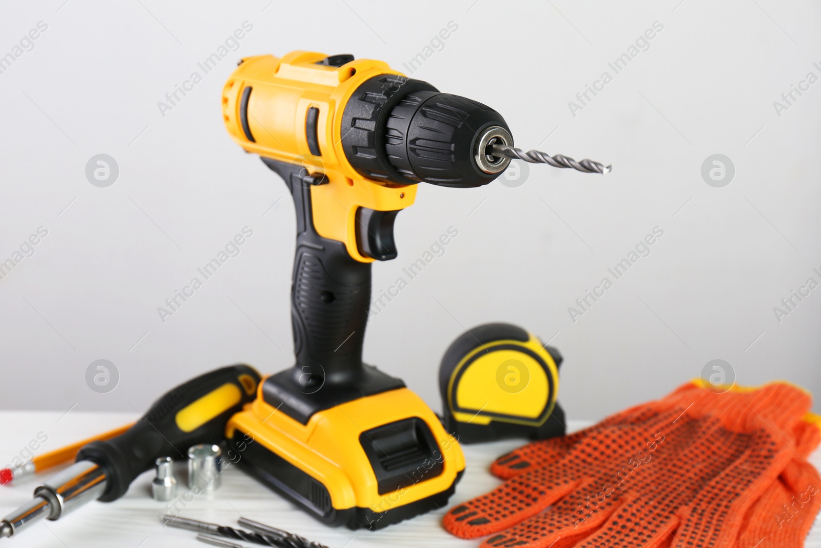 Photo of Cordless electric drill, gloves, bits, screwdriver and measuring tape on white wooden table