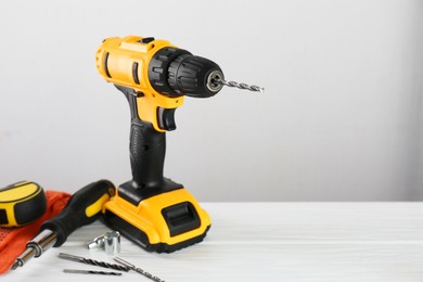 Photo of Cordless electric drill, gloves, bits, screwdriver and measuring tape on white wooden table, space for text