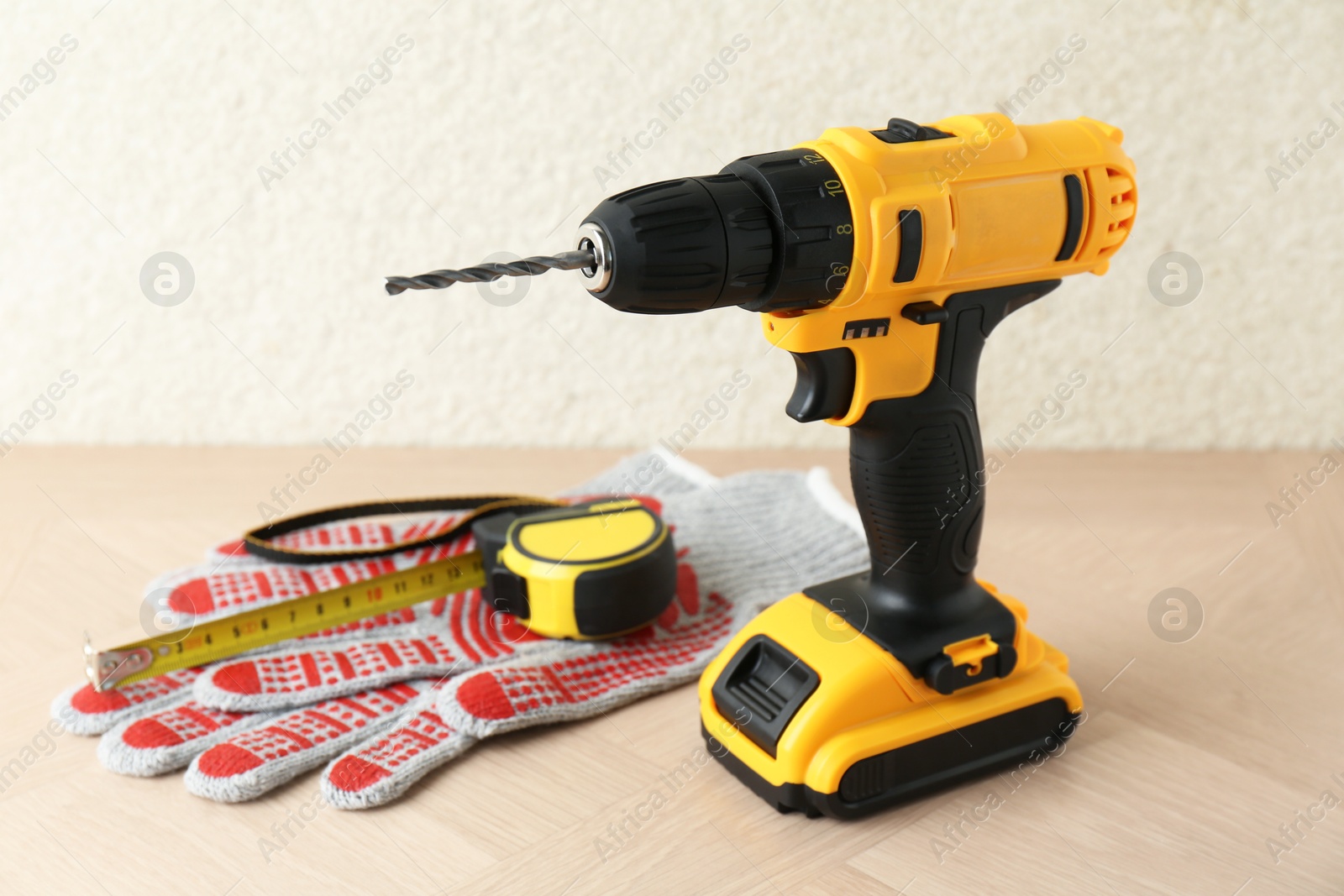 Photo of Cordless electric drill, gloves and measuring tape on wooden surface