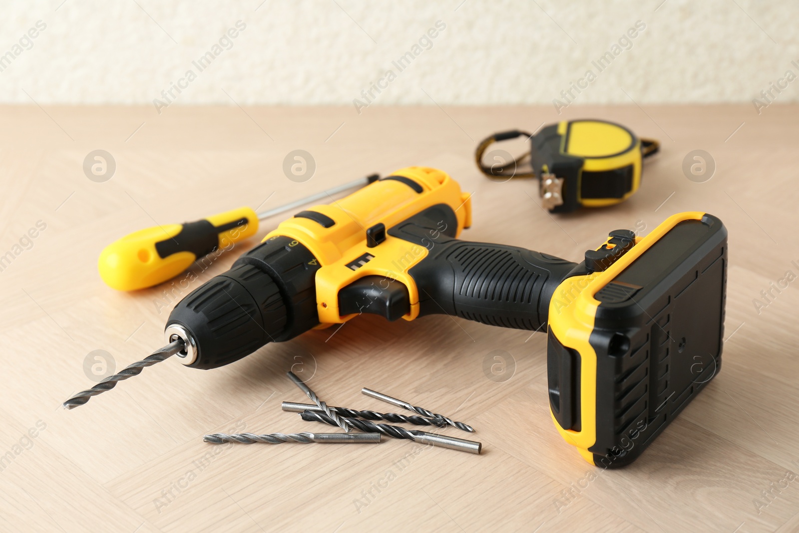 Photo of Cordless electric drill, bits, screwdriver and measuring tape on wooden surface