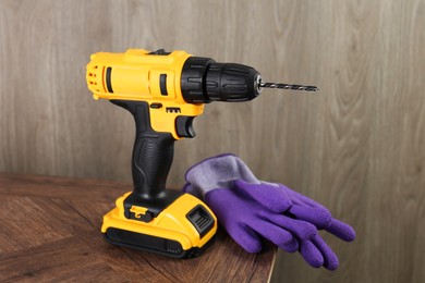 Photo of Cordless electric drill and gloves on wooden table