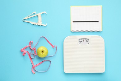 Flat lay composition with body fat caliper and scale on light blue background