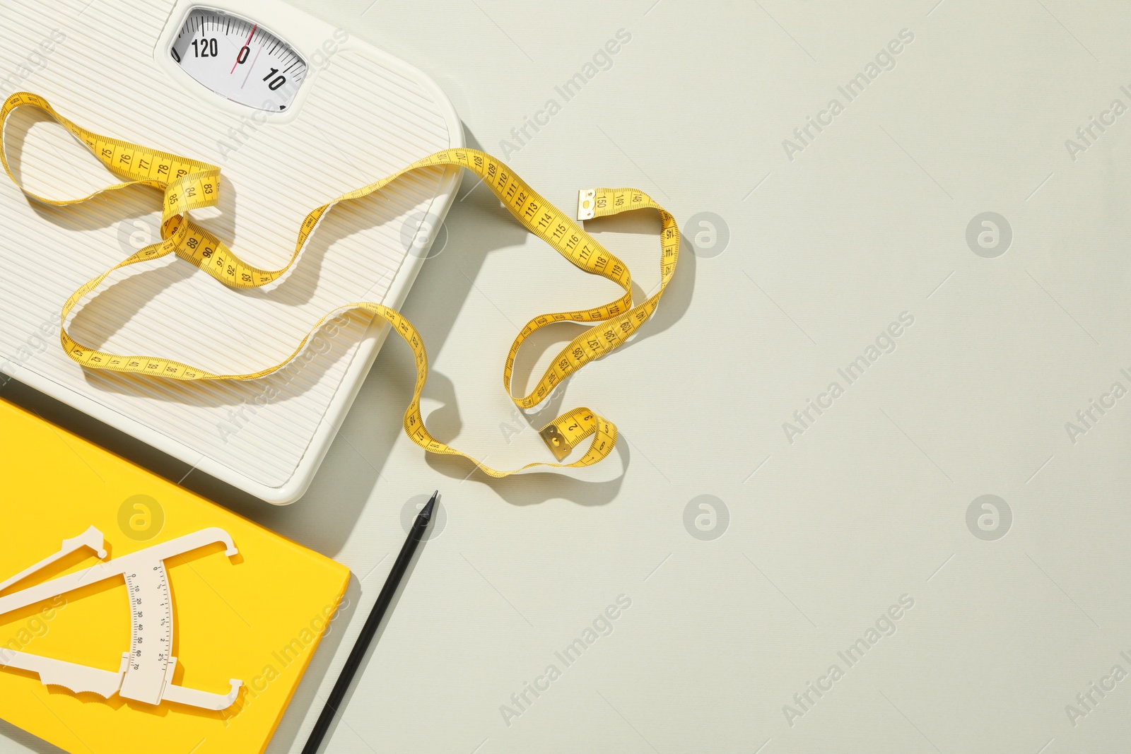 Photo of Body fat caliper, measuring tape, scale and notebook on light grey background, flat lay. Space for text