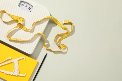 Body fat caliper, measuring tape, scale and notebook on light grey background, flat lay. Space for text