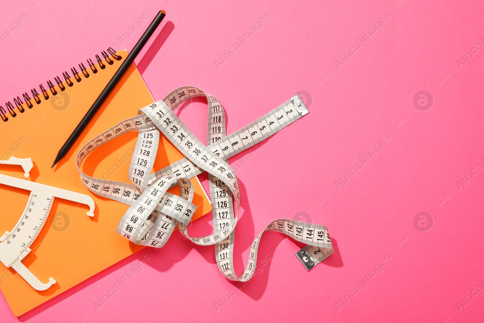 Photo of Body fat caliper, measuring tape, notebook and pencil on pink background, flat lay. Space for text