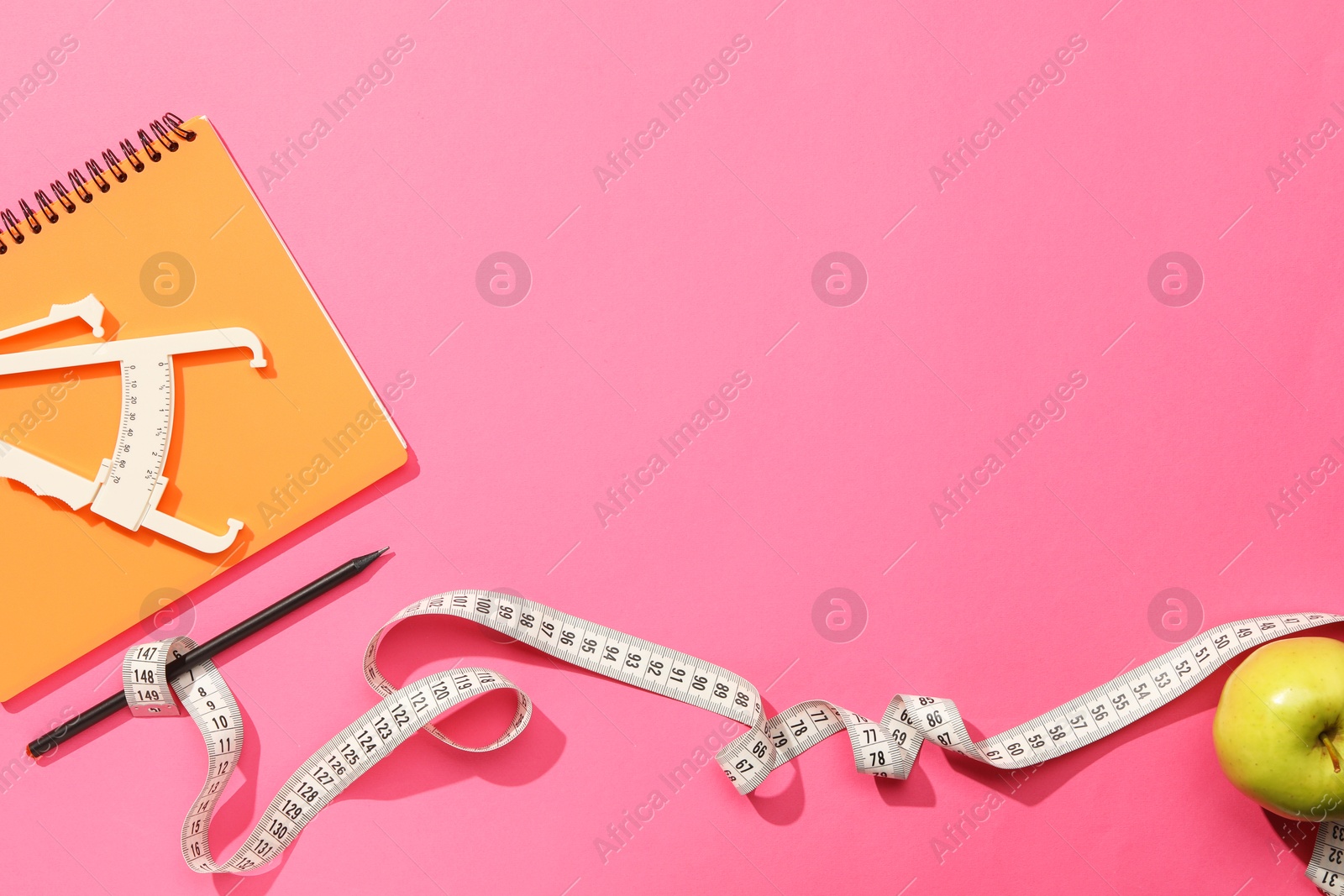 Photo of Body fat caliper, measuring tape, notebook and apple on pink background, flat lay. Space for text