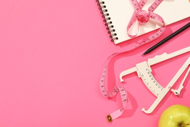 Photo of Body fat caliper, measuring tape, notebook and apple on pink background, flat lay. Space for text