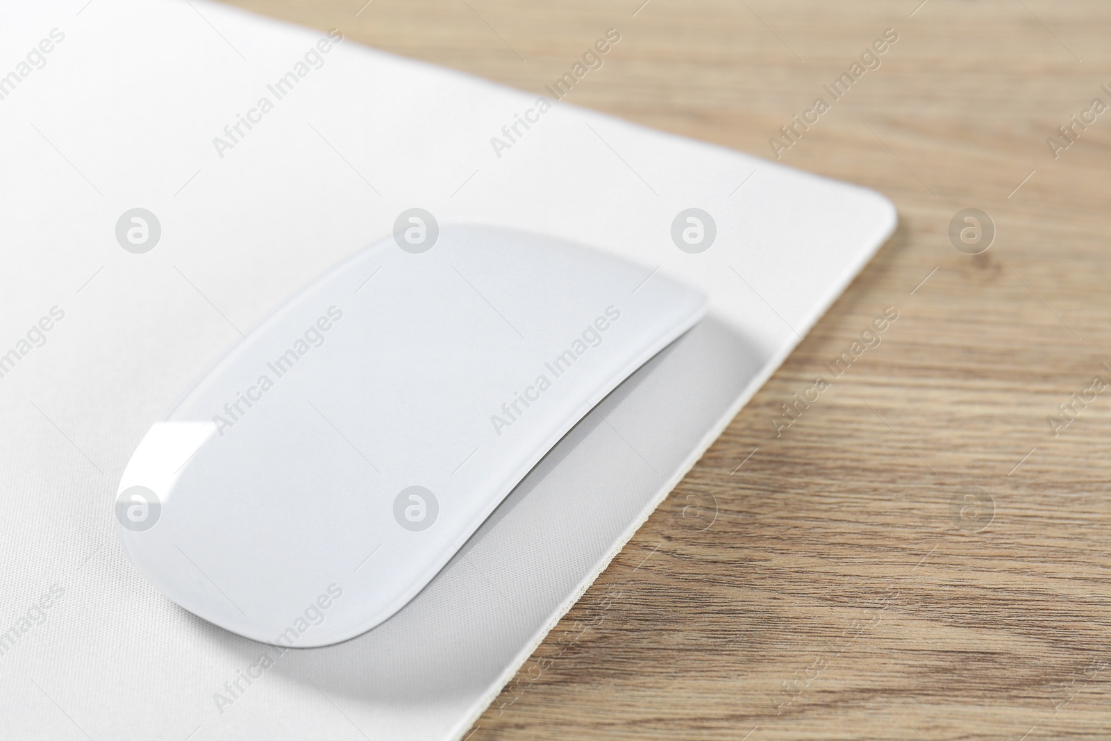 Photo of White computer mouse and mousepad on wooden table, closeup