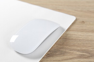 Photo of White computer mouse and mousepad on wooden table, closeup