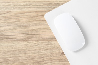 Photo of White computer mouse and mousepad on wooden table, top view