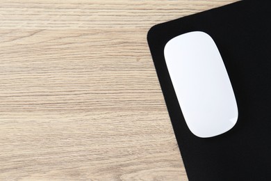 Photo of White computer mouse and black mousepad on wooden table, top view