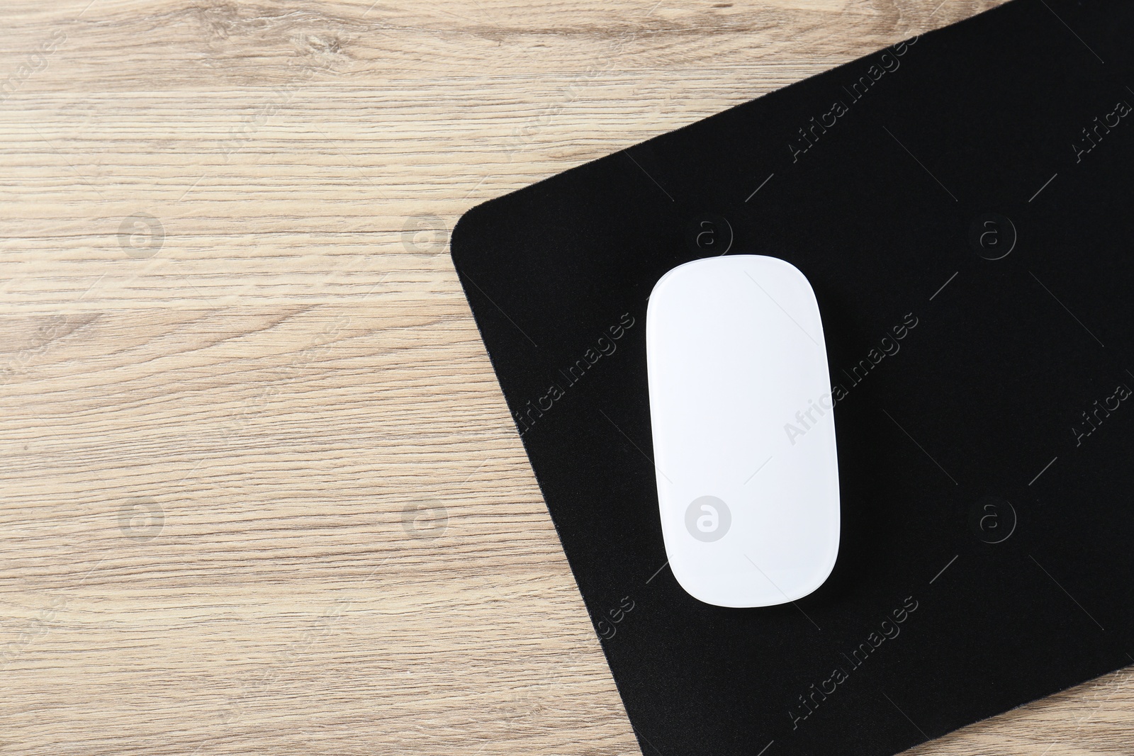 Photo of White computer mouse and black mousepad on wooden table, top view