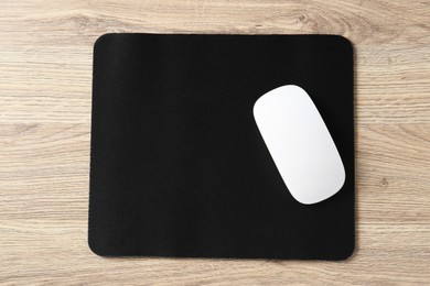 Photo of White computer mouse and black mousepad on wooden table, top view