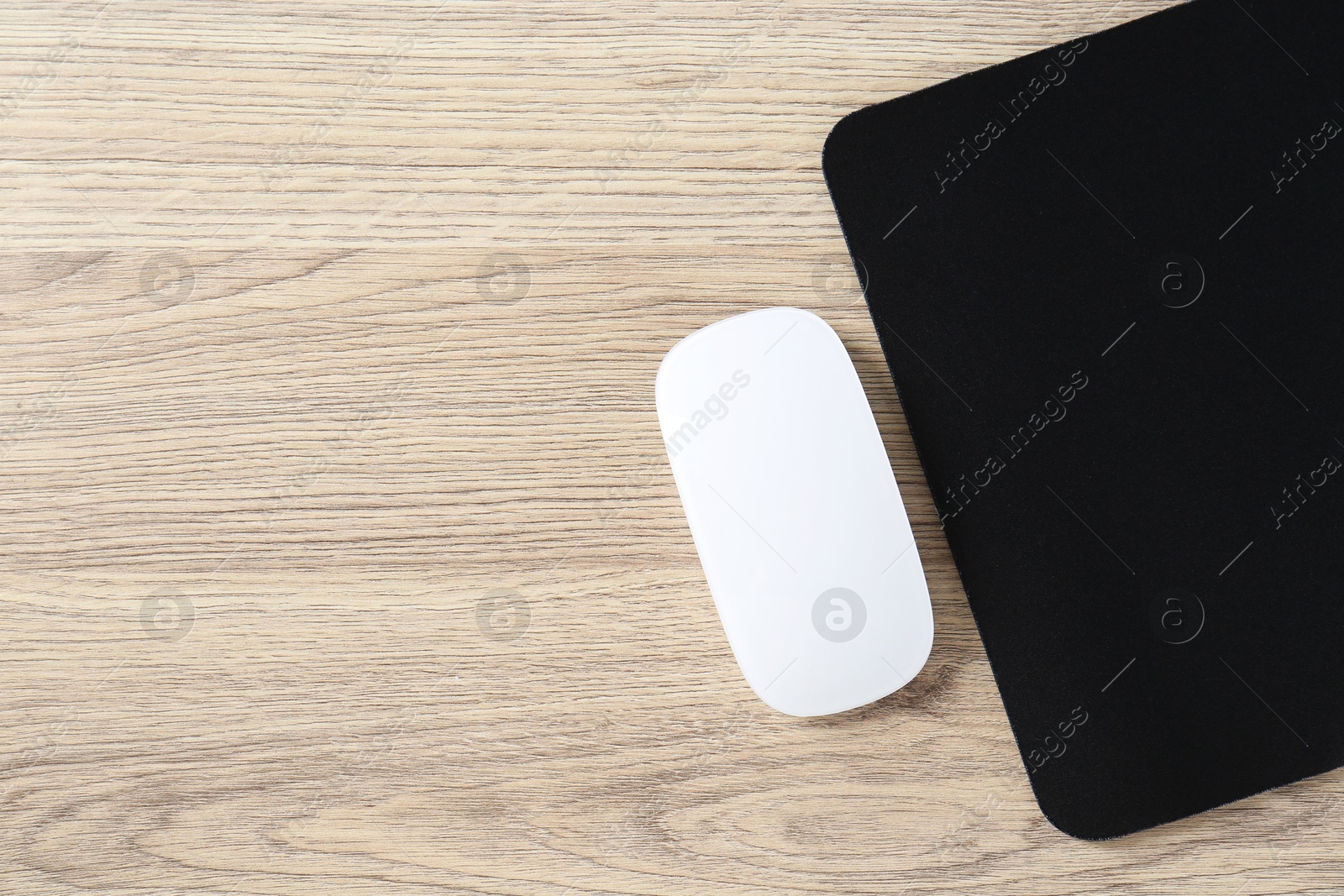 Photo of White computer mouse and black mousepad on wooden table, top view