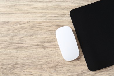 Photo of White computer mouse and black mousepad on wooden table, top view