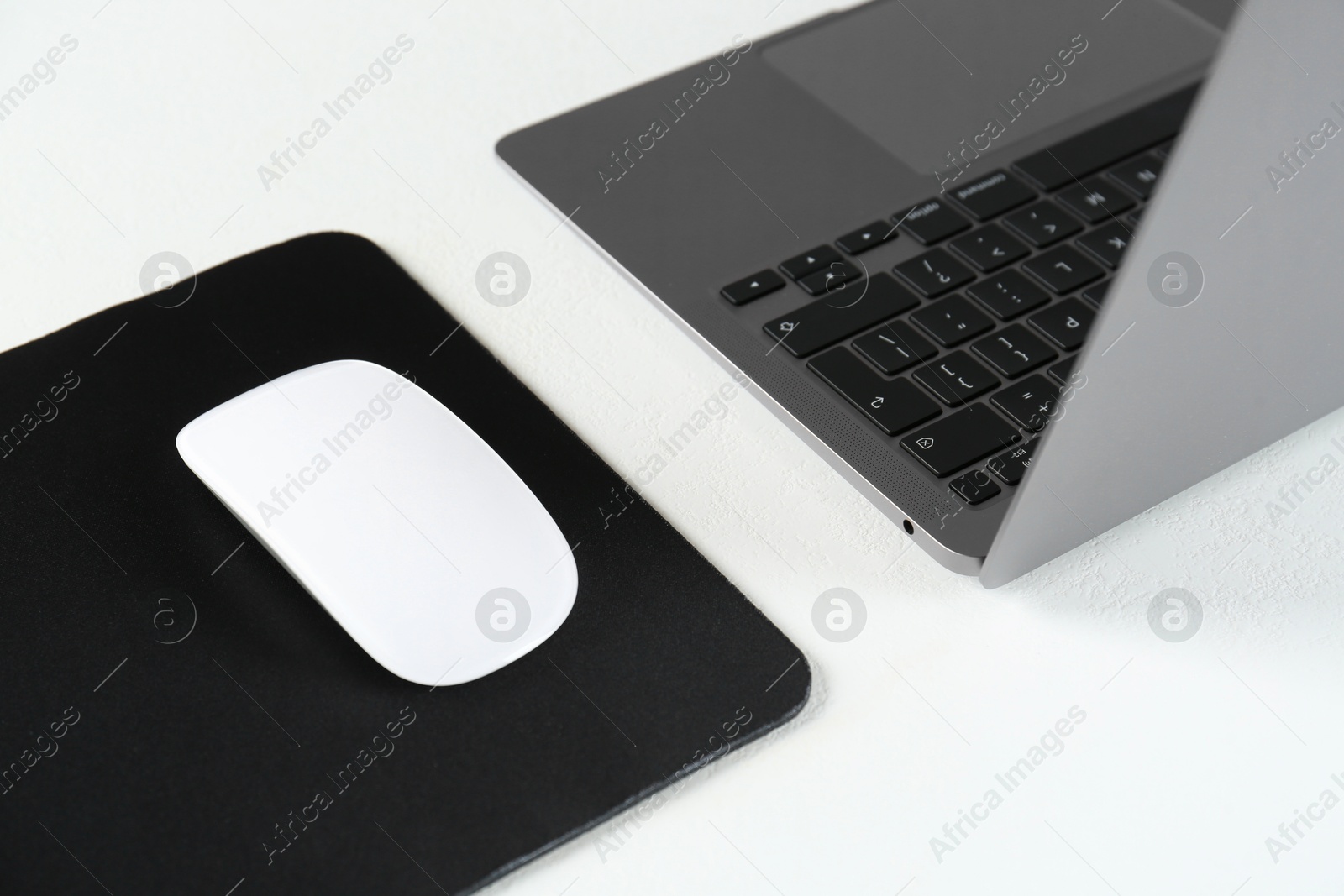 Photo of Computer mouse with mousepad and laptop on white table, closeup