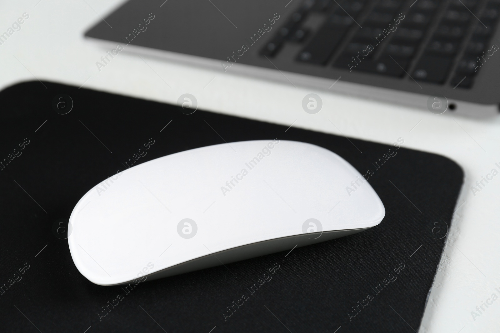 Photo of Computer mouse with mousepad and laptop on white table, closeup