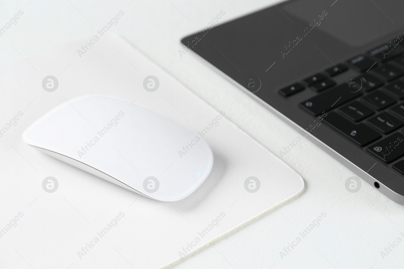 Photo of Computer mouse with mousepad and laptop on white table, closeup