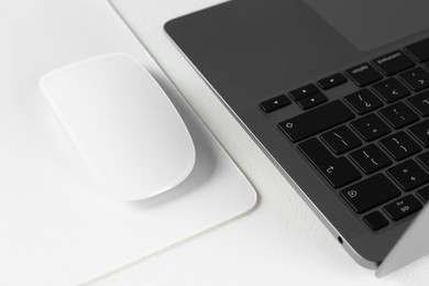 Photo of Computer mouse with mousepad and laptop on white table, closeup