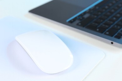 Photo of Computer mouse with mousepad and laptop on white table, closeup