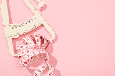 Photo of Body fat caliper and measuring tape on pink background, top view. Space for text