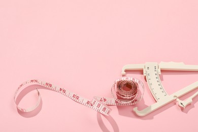 Photo of Body fat caliper and measuring tape on pink background. Space for text