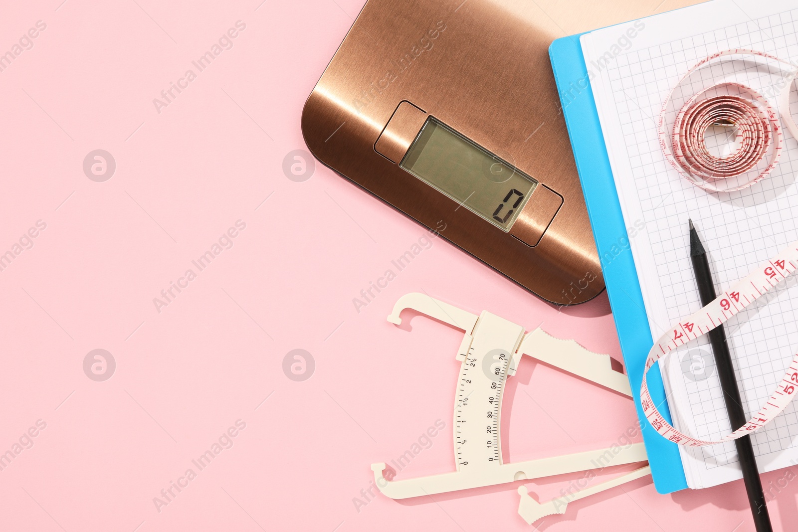 Photo of Body fat caliper, measuring tape, kitchen scale and notebook on pink background, flat lay. Space for text