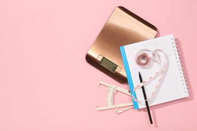 Photo of Body fat caliper, measuring tape, kitchen scale and notebook on pink background, flat lay. Space for text