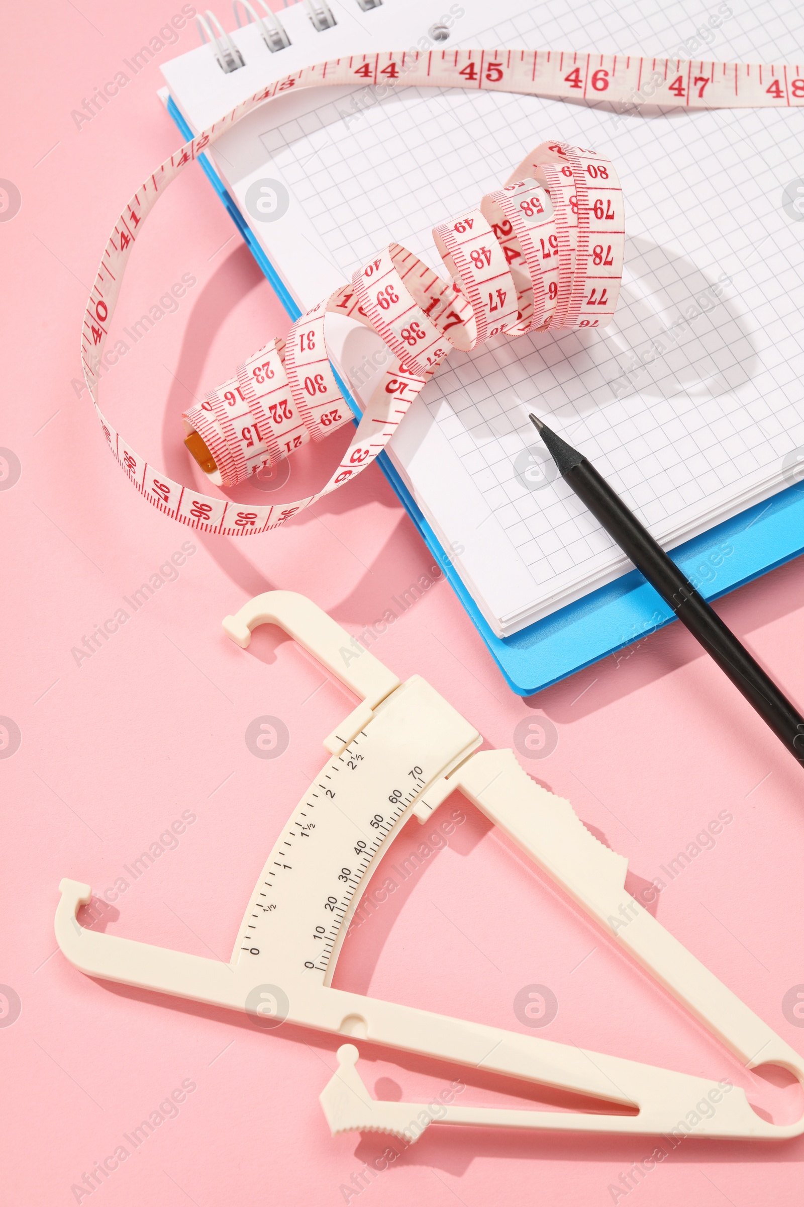 Photo of Body fat caliper, measuring tape, notebook and pencil on pink background