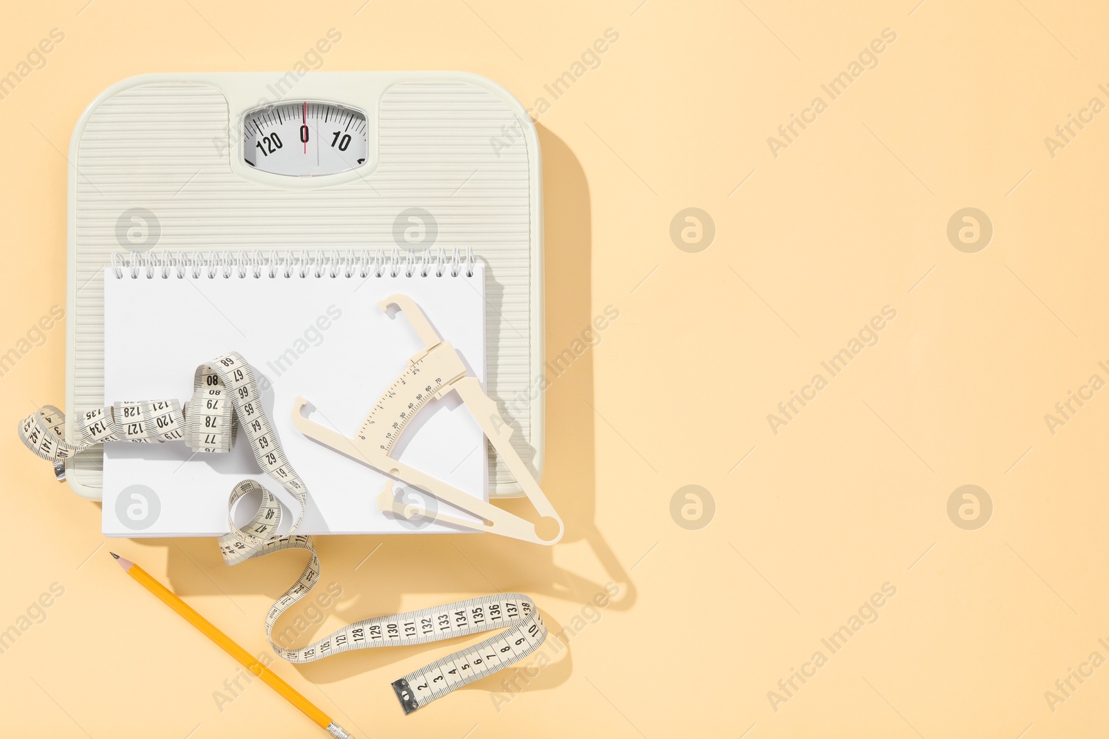 Photo of Body fat caliper, measuring tape, scale, pencil and notebook on beige background, flat lay. Space for text