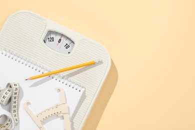 Photo of Body fat caliper, measuring tape, scale, pencil and notebook on beige background, top view. Space for text