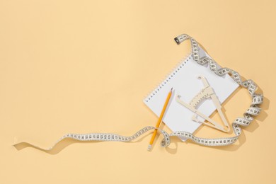 Photo of Body fat caliper, measuring tape, pencil and notebook on beige background, flat lay. Space for text