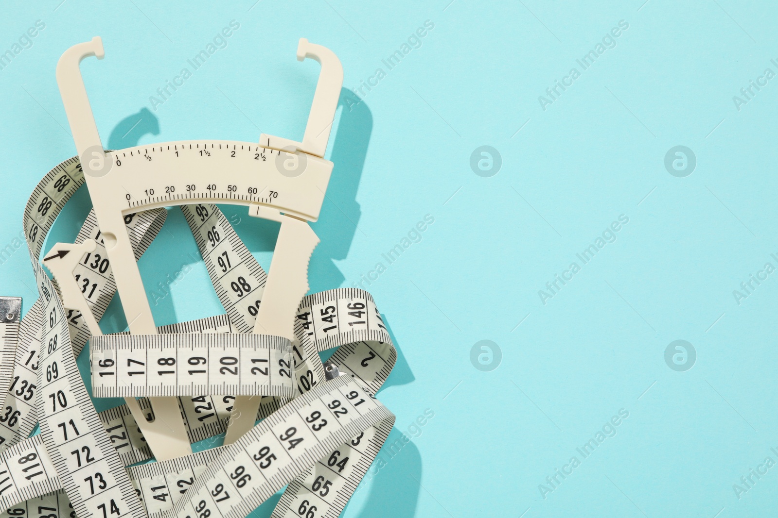 Photo of Plastic body fat caliper and measuring tape on light blue background, top view. Space for text