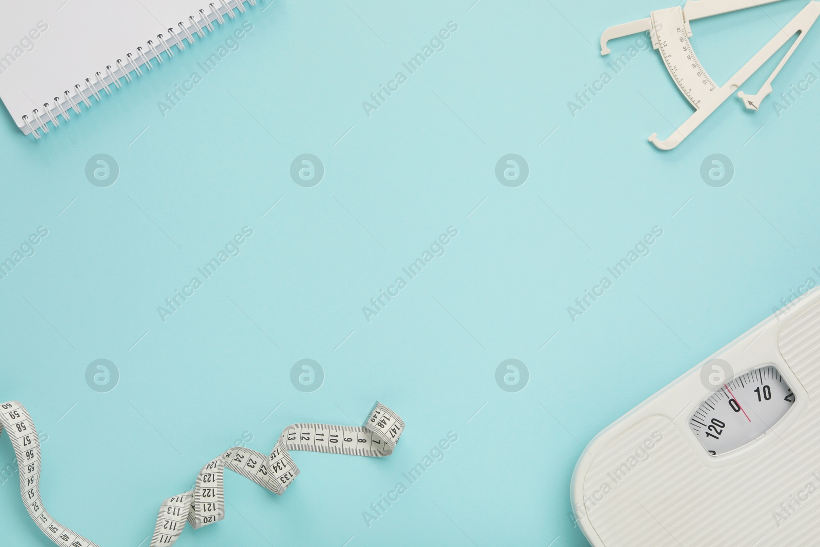 Photo of Body fat caliper, measuring tape, scale and notebook on light blue background, flat lay. Space for text