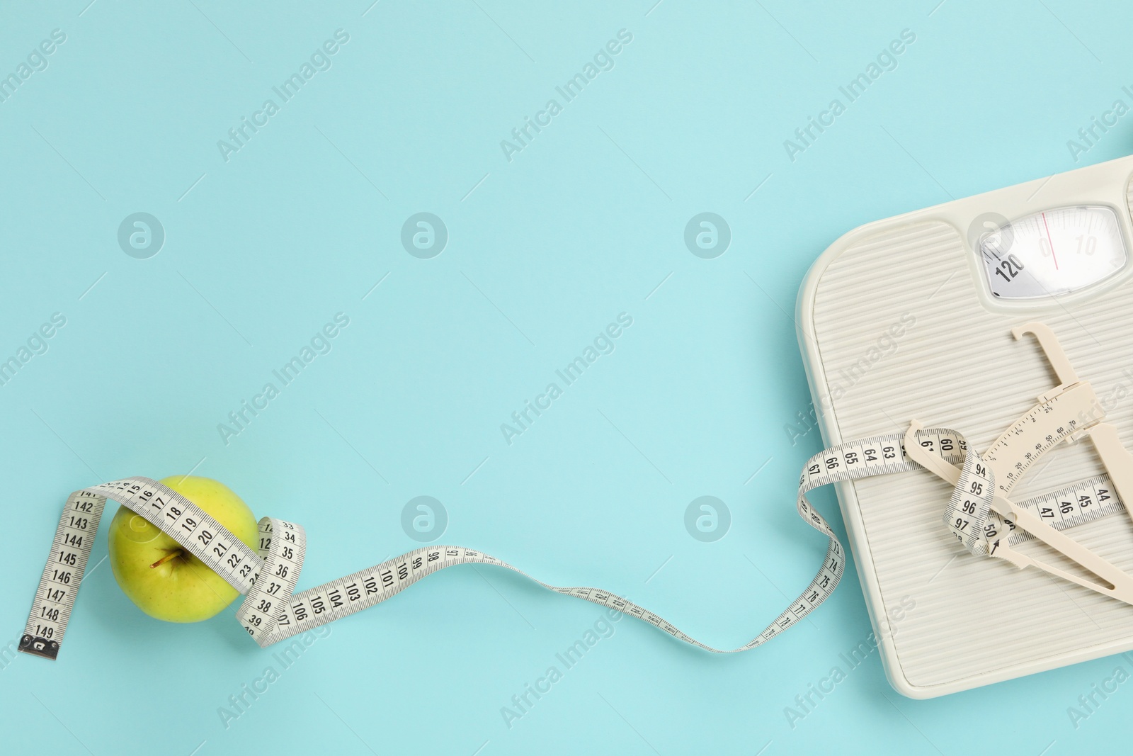 Photo of Body fat caliper, measuring tape, apple and notebook on light blue background, flat lay. Space for text