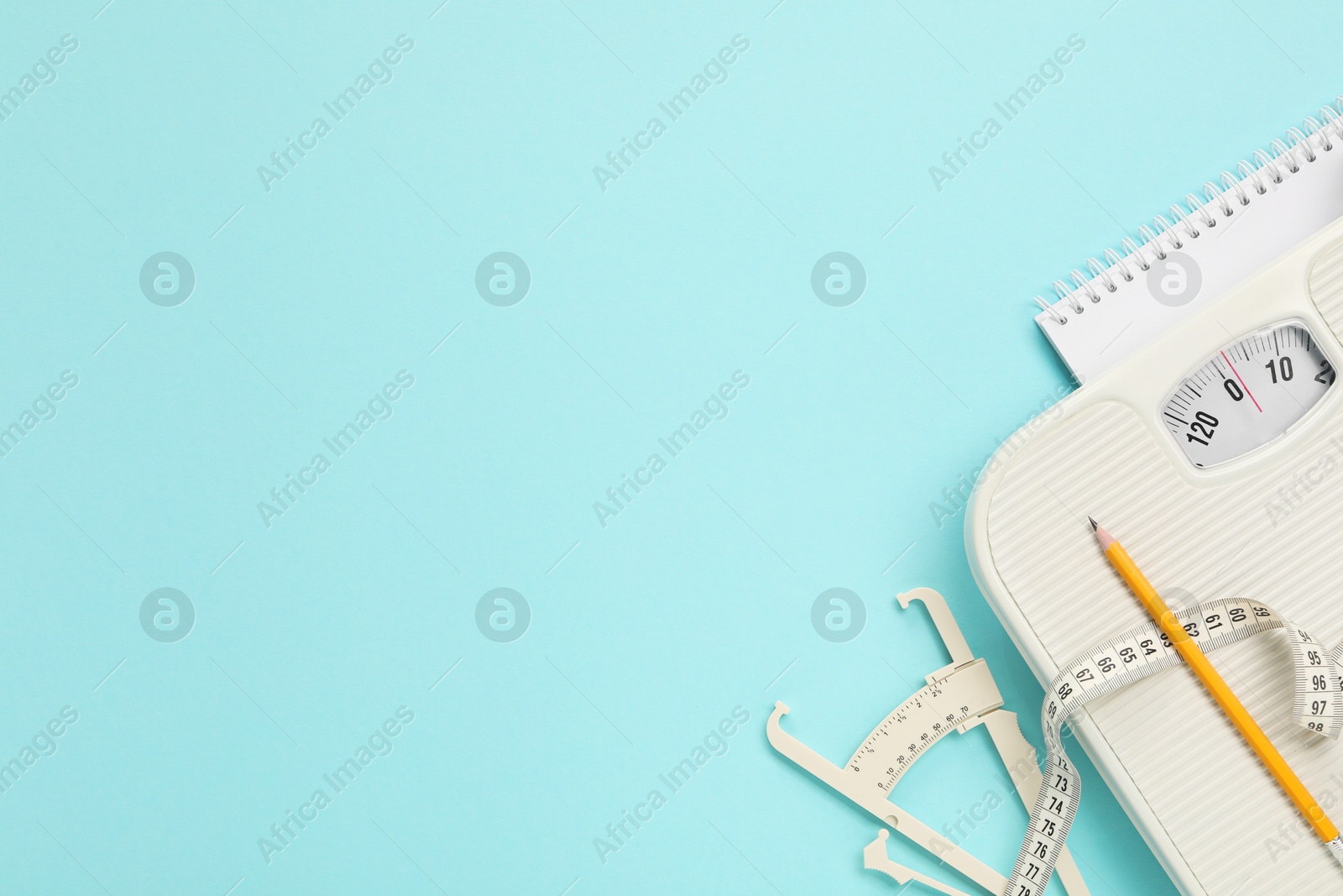 Photo of Body fat caliper, measuring tape, scale, pencil and notebook on light blue background, flat lay. Space for text