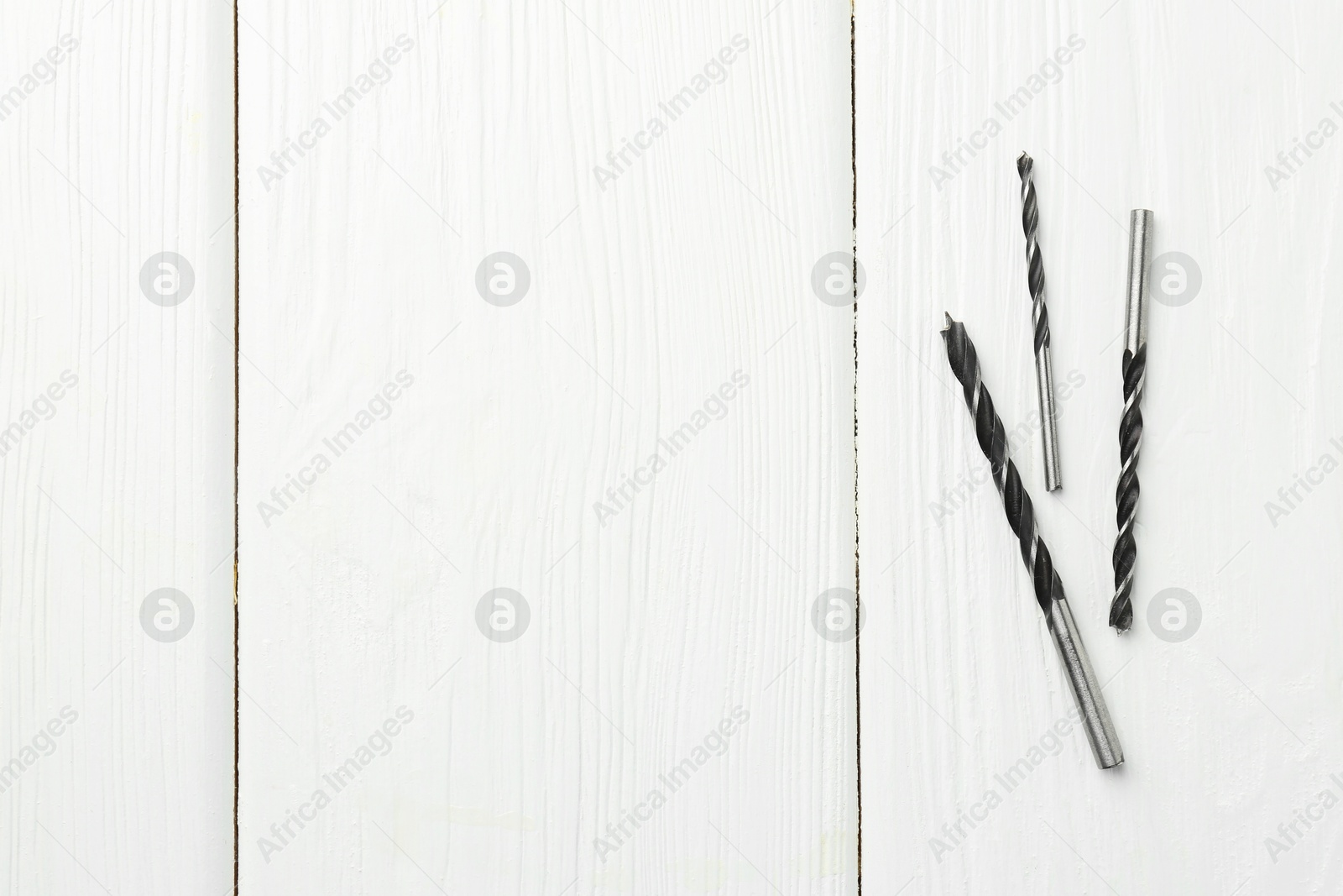 Photo of Different drill bits on white wooden table, top view. Space for text