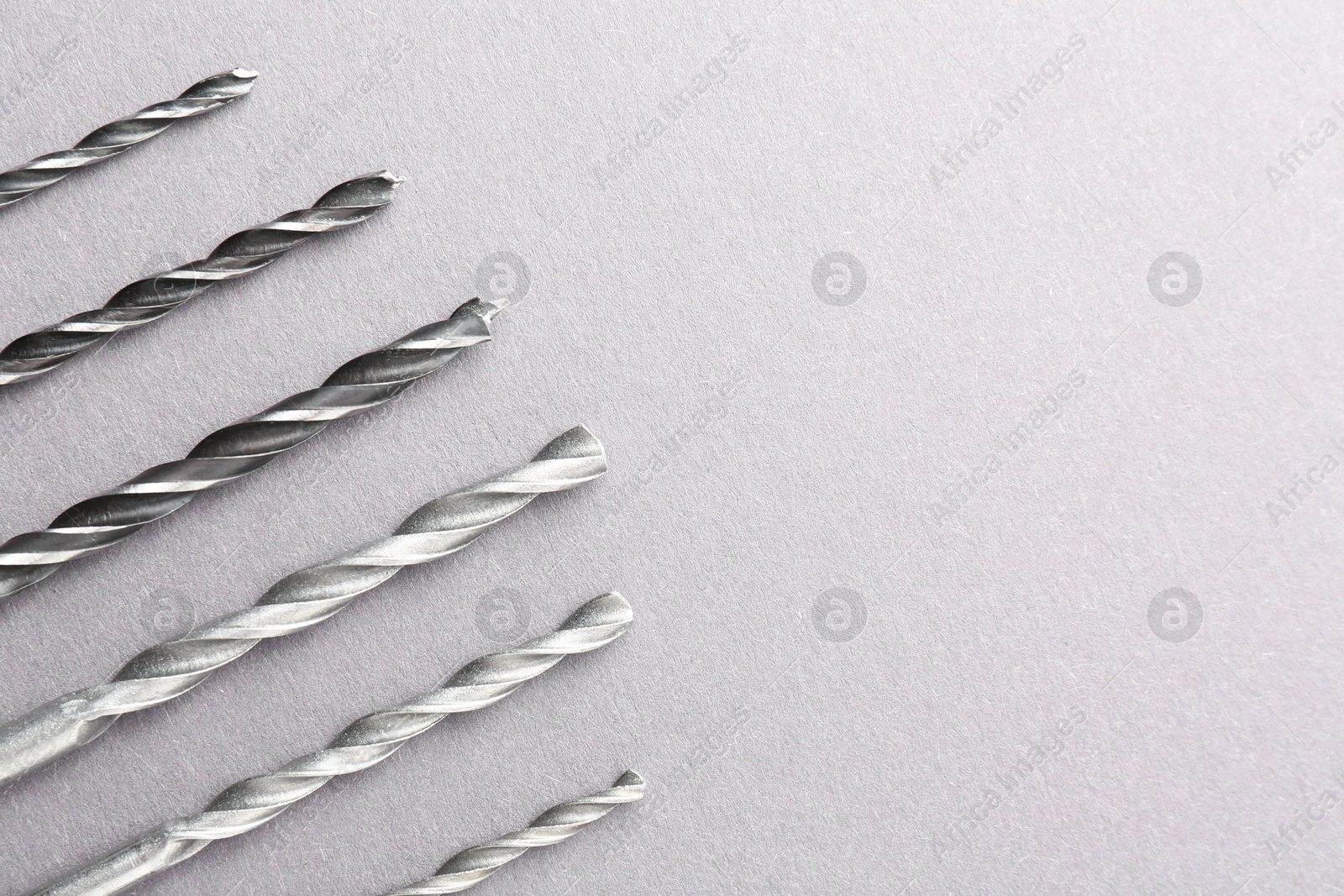 Photo of Many different drill bits on light grey table, top view. Space for text