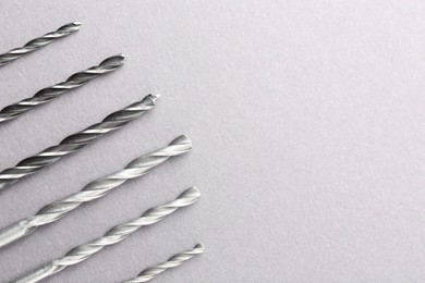 Photo of Many different drill bits on light grey table, top view. Space for text