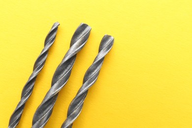 Photo of Different drill bits on yellow background, top view. Space for text