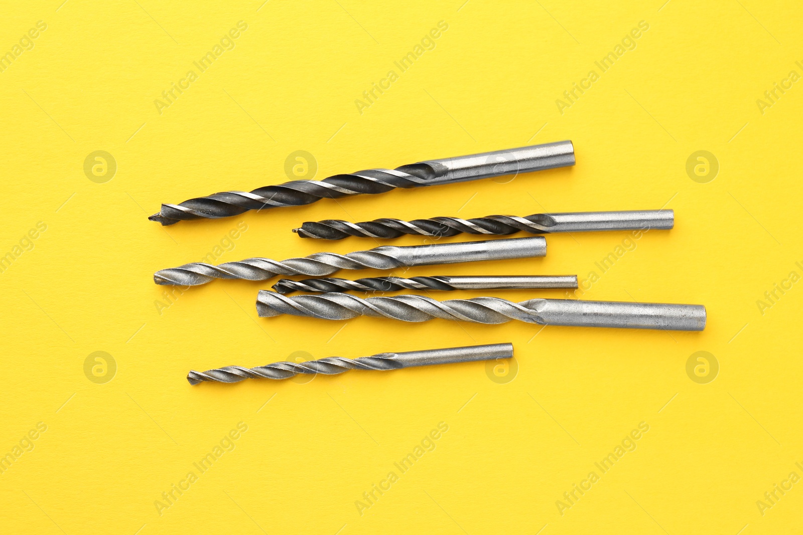 Photo of Many different drill bits on yellow background, top view