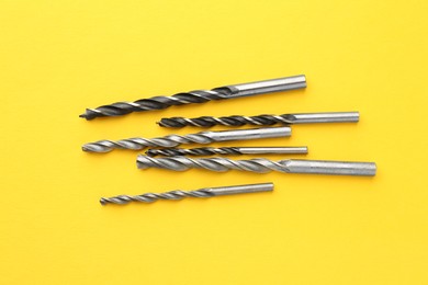 Photo of Many different drill bits on yellow background, top view