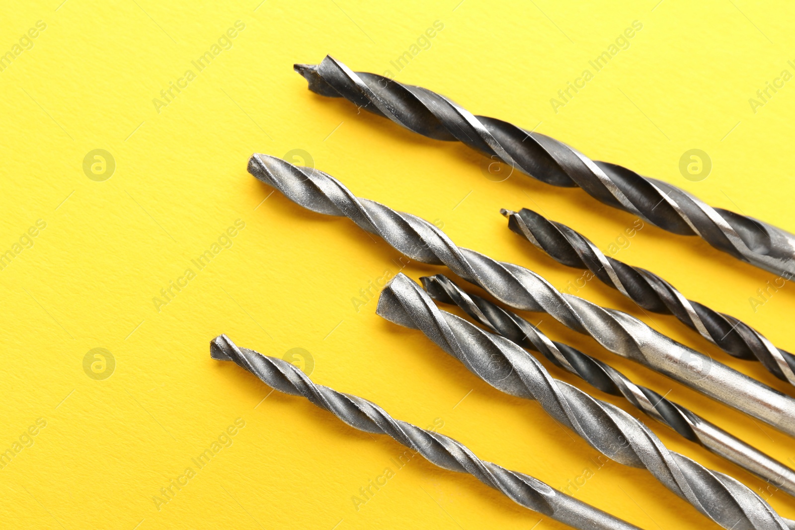 Photo of Many different drill bits on yellow background, top view