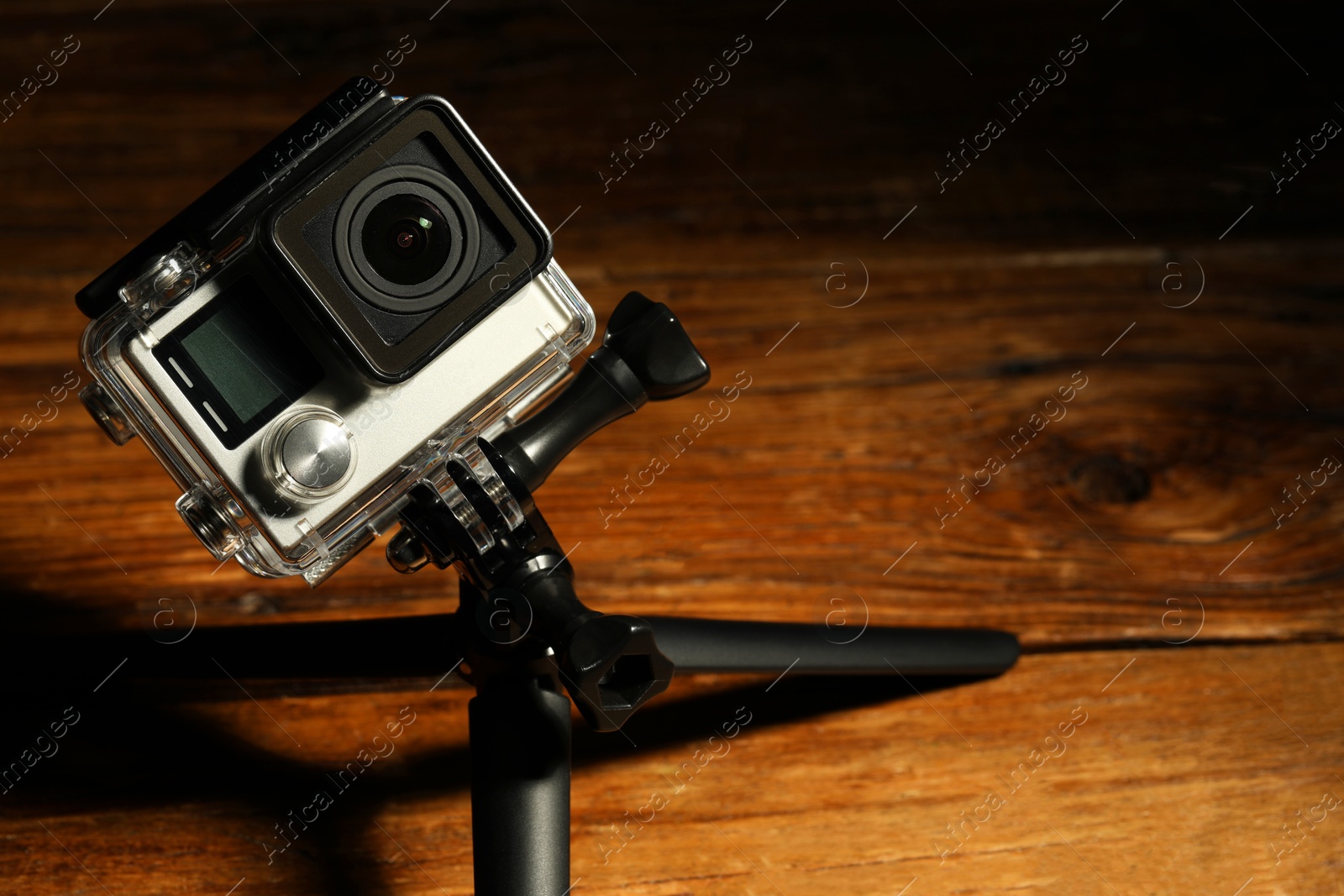 Photo of Modern action camera and tripod on wooden surface. Space for text