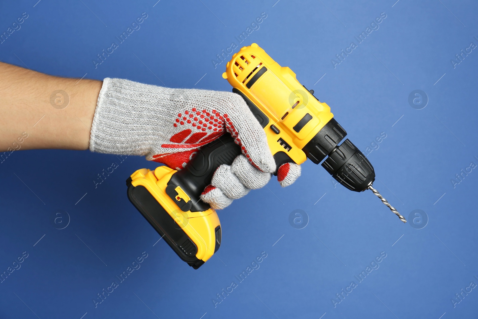 Photo of Man with cordless electric drill on blue background, closeup