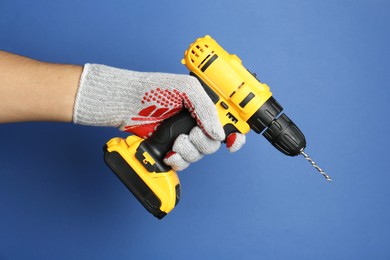 Photo of Man with cordless electric drill on blue background, closeup