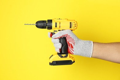 Photo of Man with cordless electric drill on yellow background, closeup