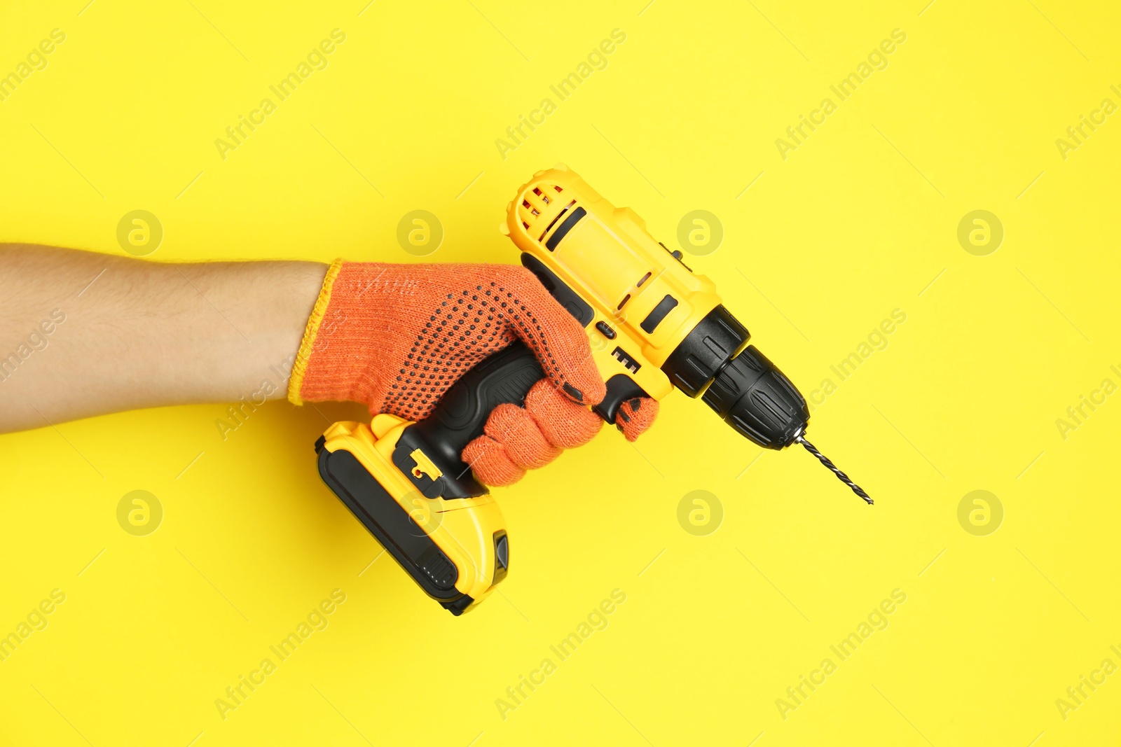 Photo of Man with cordless electric drill on yellow background, closeup