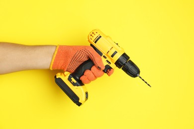 Photo of Man with cordless electric drill on yellow background, closeup