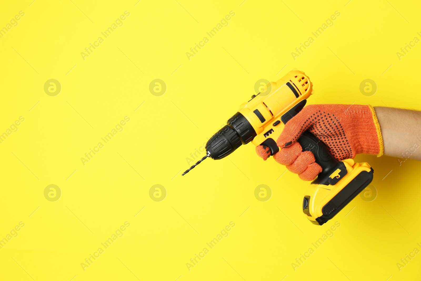 Photo of Man with cordless electric drill on yellow background, closeup. Space for text